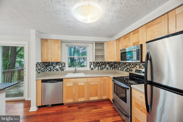 kitchen featuring stainless steel appliances, a sink, light brown cabinetry, a textured ceiling, and dark wood finished floors