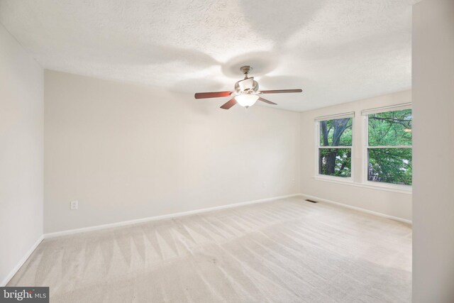 unfurnished room featuring baseboards, light carpet, ceiling fan, and a textured ceiling