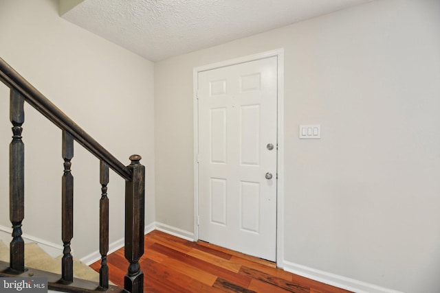 foyer featuring wood finished floors, baseboards, stairway, and a textured ceiling