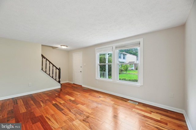 foyer entrance featuring stairs, baseboards, wood finished floors, and a textured ceiling