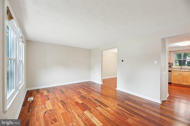 empty room with a sink, light wood finished floors, a textured ceiling, and baseboards