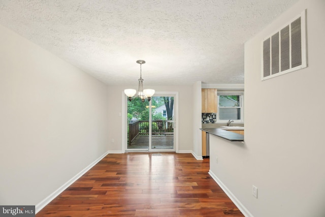 unfurnished dining area with a chandelier, dark wood finished floors, baseboards, a textured ceiling, and a sink