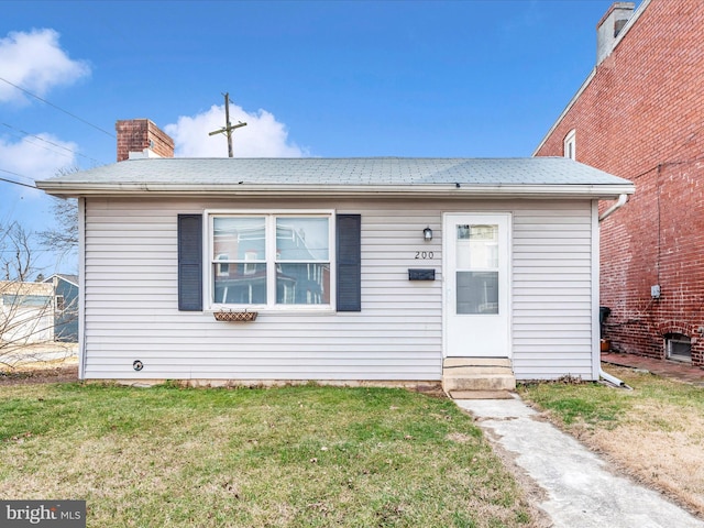 bungalow-style home with a front yard, a chimney, and entry steps