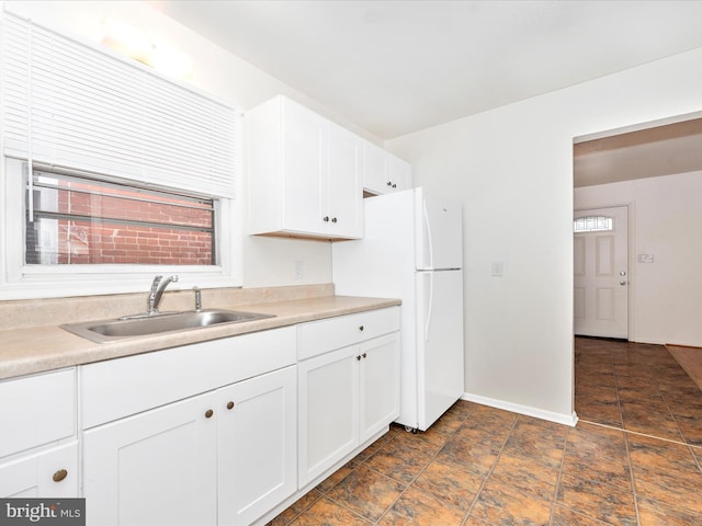 kitchen with baseboards, freestanding refrigerator, light countertops, white cabinetry, and a sink