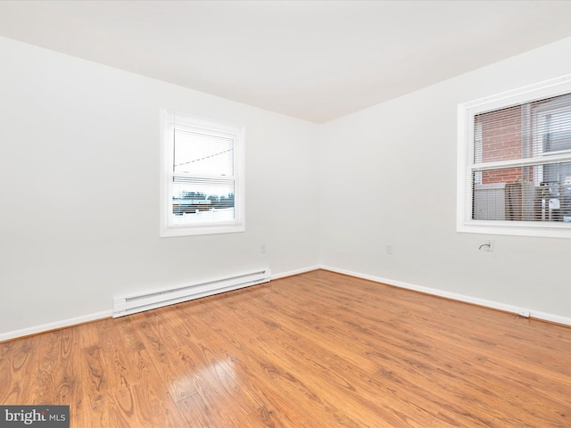 spare room with baseboard heating, wood finished floors, and baseboards