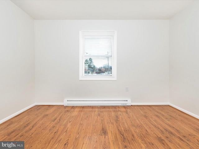 spare room with a baseboard heating unit, baseboards, and wood finished floors