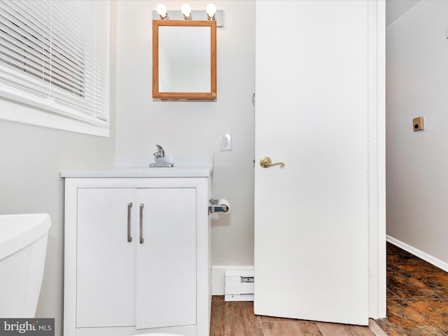 half bath featuring toilet, baseboard heating, vanity, and baseboards