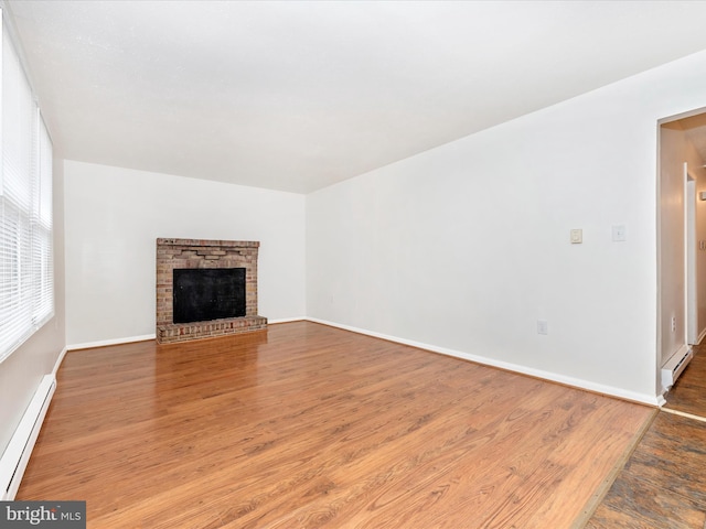 unfurnished living room featuring a baseboard heating unit, a fireplace, baseboards, and wood finished floors