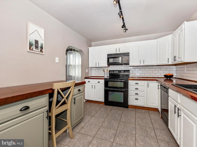 kitchen with black appliances, arched walkways, butcher block counters, light tile patterned floors, and decorative backsplash