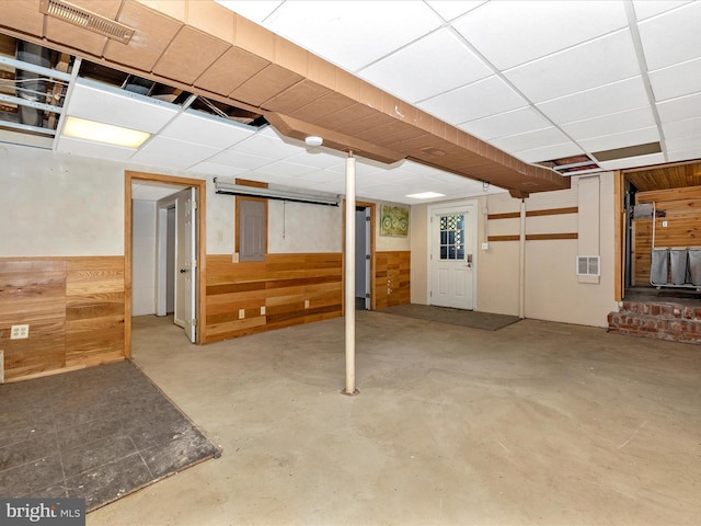 finished below grade area with visible vents, a paneled ceiling, wood walls, and wainscoting