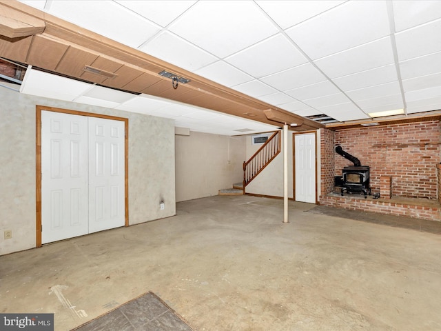 finished basement featuring stairway, a wood stove, and a paneled ceiling