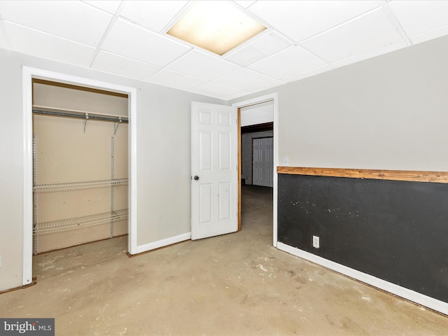 unfurnished bedroom featuring unfinished concrete floors, a paneled ceiling, baseboards, and a closet