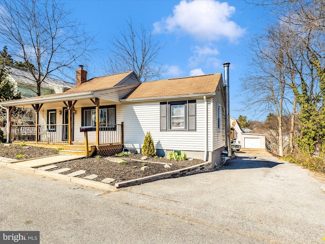 view of front of home with driveway, covered porch, an outdoor structure, a shingled roof, and a chimney