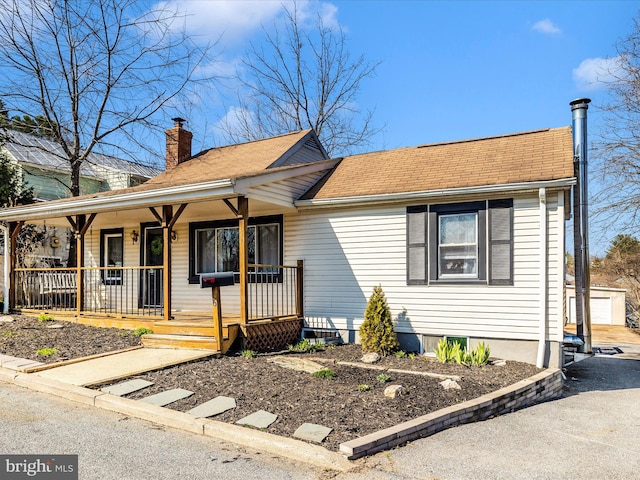 ranch-style house featuring an outbuilding, covered porch, a chimney, and a shingled roof