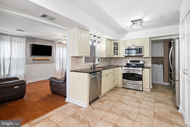 kitchen featuring visible vents, cream cabinetry, a sink, open floor plan, and appliances with stainless steel finishes