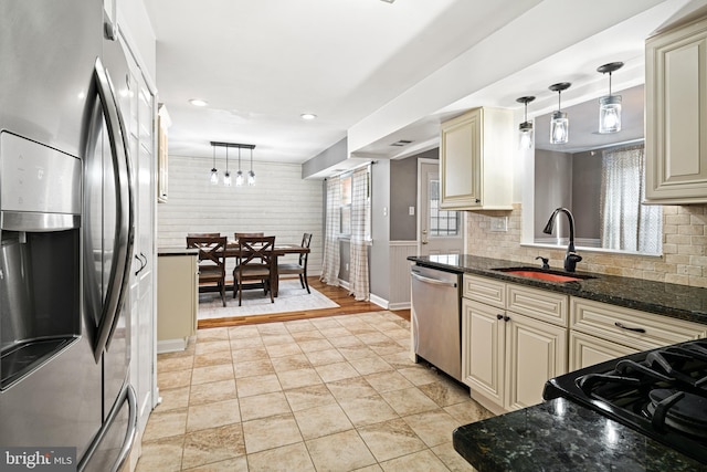 kitchen with a sink, cream cabinets, decorative light fixtures, and stainless steel appliances