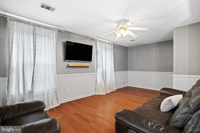 living area featuring visible vents, wood finished floors, ceiling fan, and wainscoting