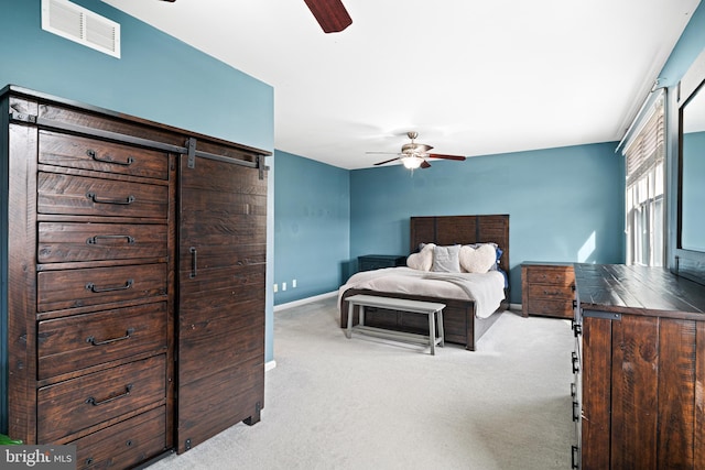 carpeted bedroom with visible vents, baseboards, a barn door, and a ceiling fan