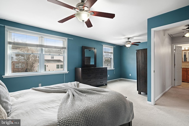 bedroom with ensuite bath, light colored carpet, a ceiling fan, and baseboards