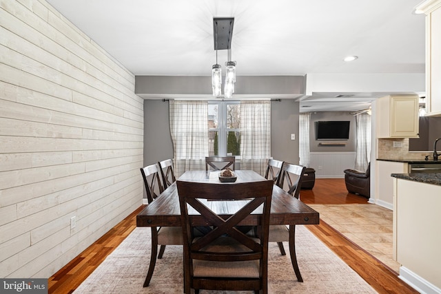 dining room with wooden walls, recessed lighting, and light wood-type flooring