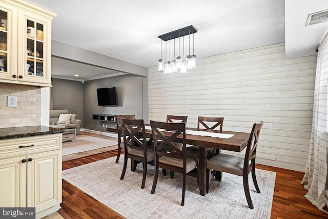 dining area with dark wood finished floors, wood walls, crown molding, and baseboards