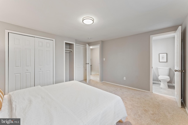 bedroom with light carpet, baseboards, ensuite bathroom, and multiple closets