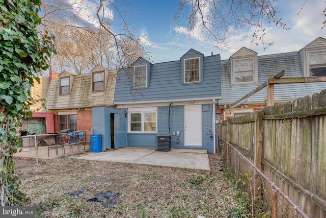 rear view of property featuring a patio, brick siding, mansard roof, and a fenced backyard