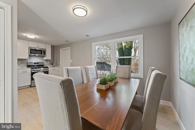 dining room featuring light wood-type flooring, visible vents, and baseboards