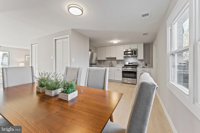 dining area featuring light wood-type flooring, visible vents, and baseboards