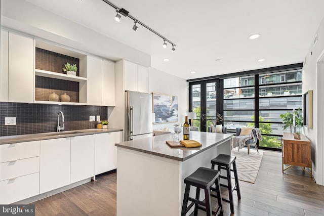 kitchen with decorative backsplash, a breakfast bar area, high end fridge, a wall of windows, and a sink