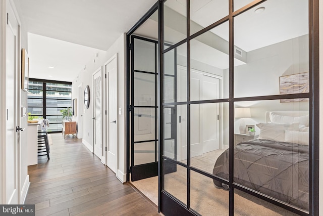 corridor with baseboards, visible vents, wood finished floors, a wall of windows, and french doors