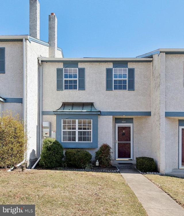 townhome / multi-family property with a front yard, a chimney, and stucco siding