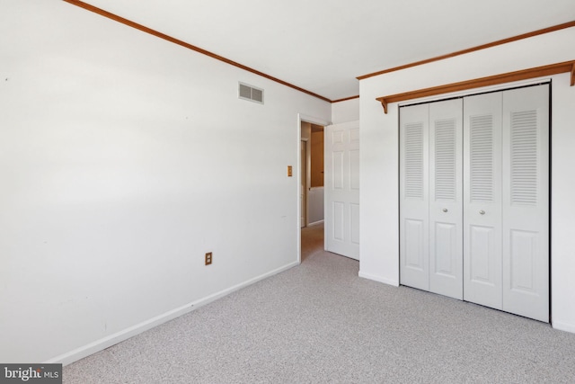 unfurnished bedroom with visible vents, baseboards, ornamental molding, carpet floors, and a closet