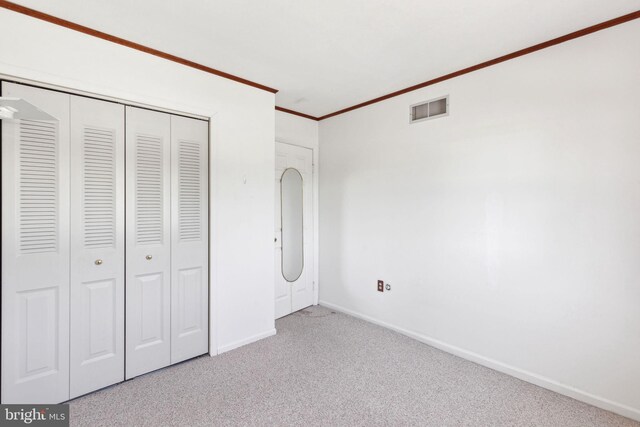 unfurnished bedroom featuring baseboards, visible vents, a closet, crown molding, and carpet flooring