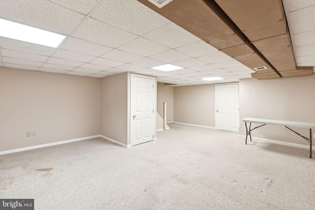 finished below grade area featuring a drop ceiling, visible vents, carpet floors, and baseboards