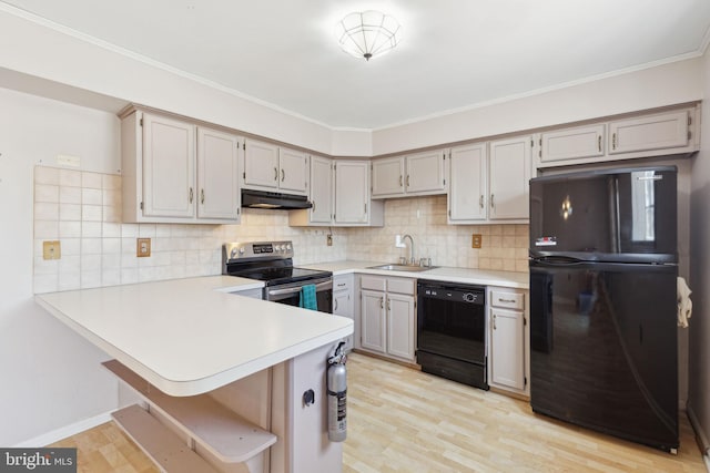 kitchen featuring black appliances, a sink, under cabinet range hood, light countertops, and decorative backsplash