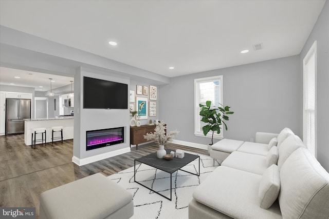 living area featuring visible vents, baseboards, a glass covered fireplace, wood finished floors, and recessed lighting