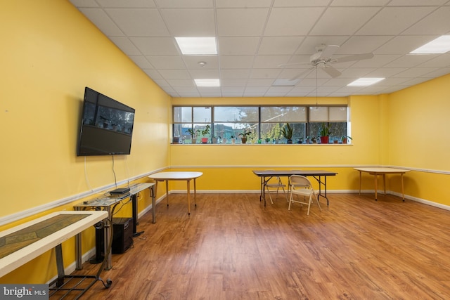 interior space featuring ceiling fan, a drop ceiling, wood finished floors, and baseboards