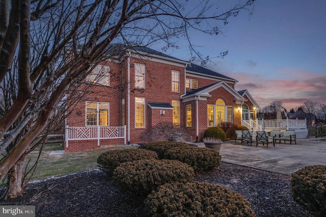 view of front of home with driveway, brick siding, and a patio area