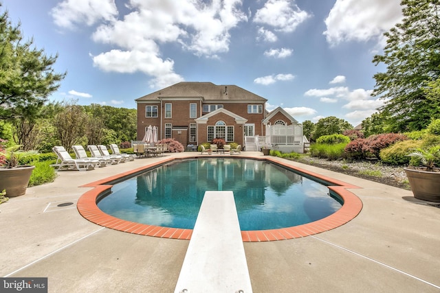 outdoor pool with a diving board and a patio area