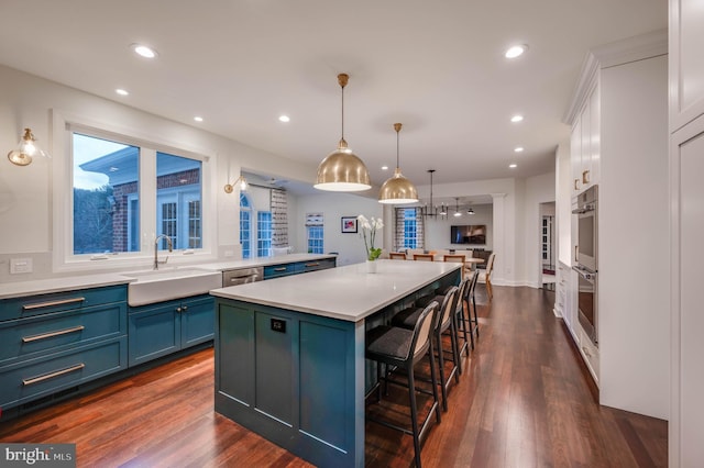 kitchen featuring a center island, light countertops, stainless steel double oven, blue cabinetry, and a sink