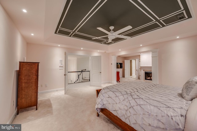 bedroom featuring baseboards, light colored carpet, a lit fireplace, a tray ceiling, and recessed lighting