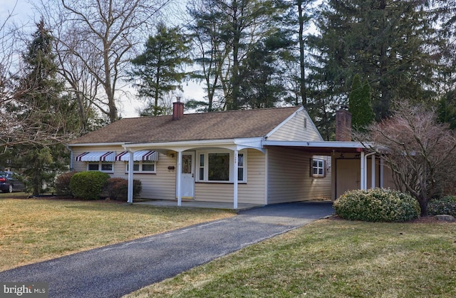 ranch-style home featuring driveway, an attached carport, a chimney, and a front yard