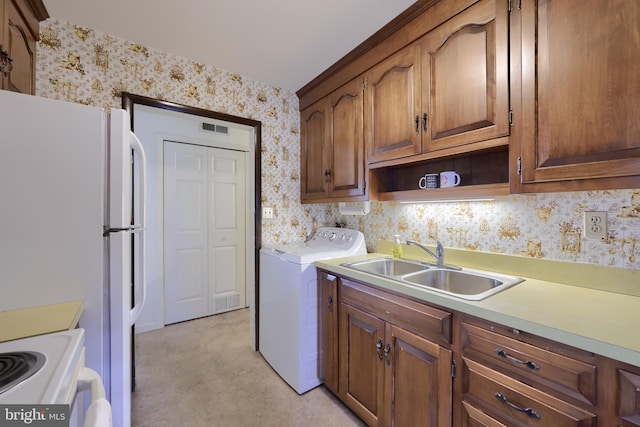 kitchen with a sink, light countertops, freestanding refrigerator, washer / clothes dryer, and wallpapered walls