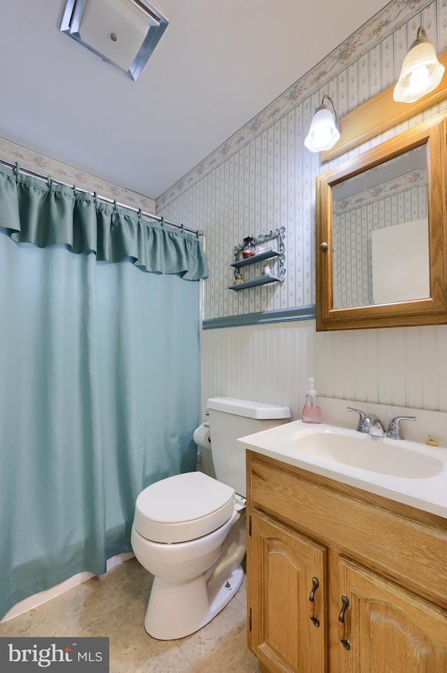 full bathroom featuring toilet, a shower with shower curtain, vanity, wainscoting, and wallpapered walls