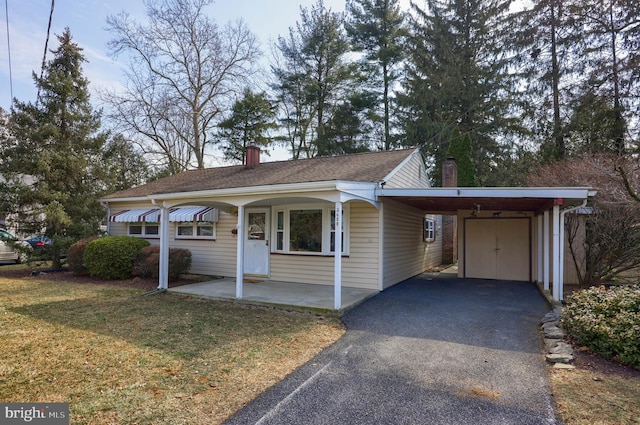 view of front of property featuring a carport, a front yard, a chimney, and aphalt driveway