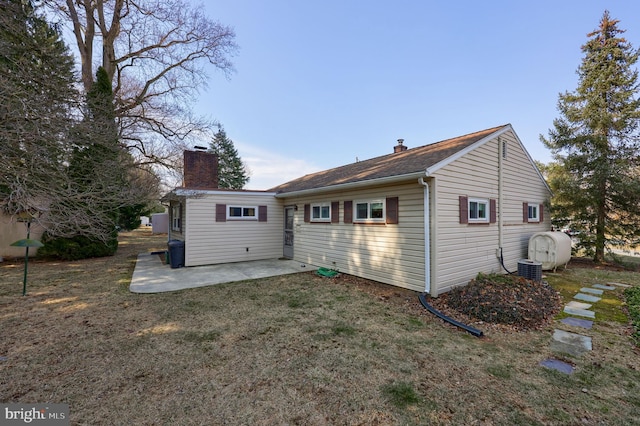 rear view of property featuring a chimney, a patio area, and a lawn