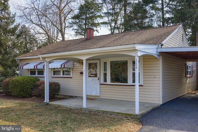 view of front of property with a shingled roof, a chimney, and an attached carport