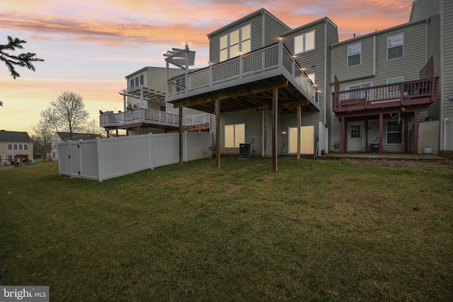 back of house at dusk with central air condition unit, a wooden deck, fence, and a yard