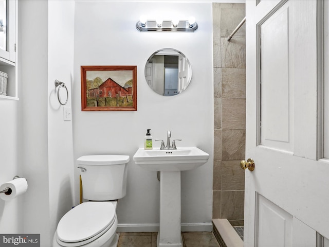 full bath featuring baseboards, toilet, tiled shower, and a sink